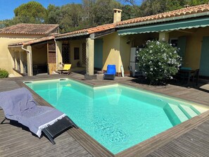 Una piscina con un solarium in legno, poltroncine da relax e una zona porticata.