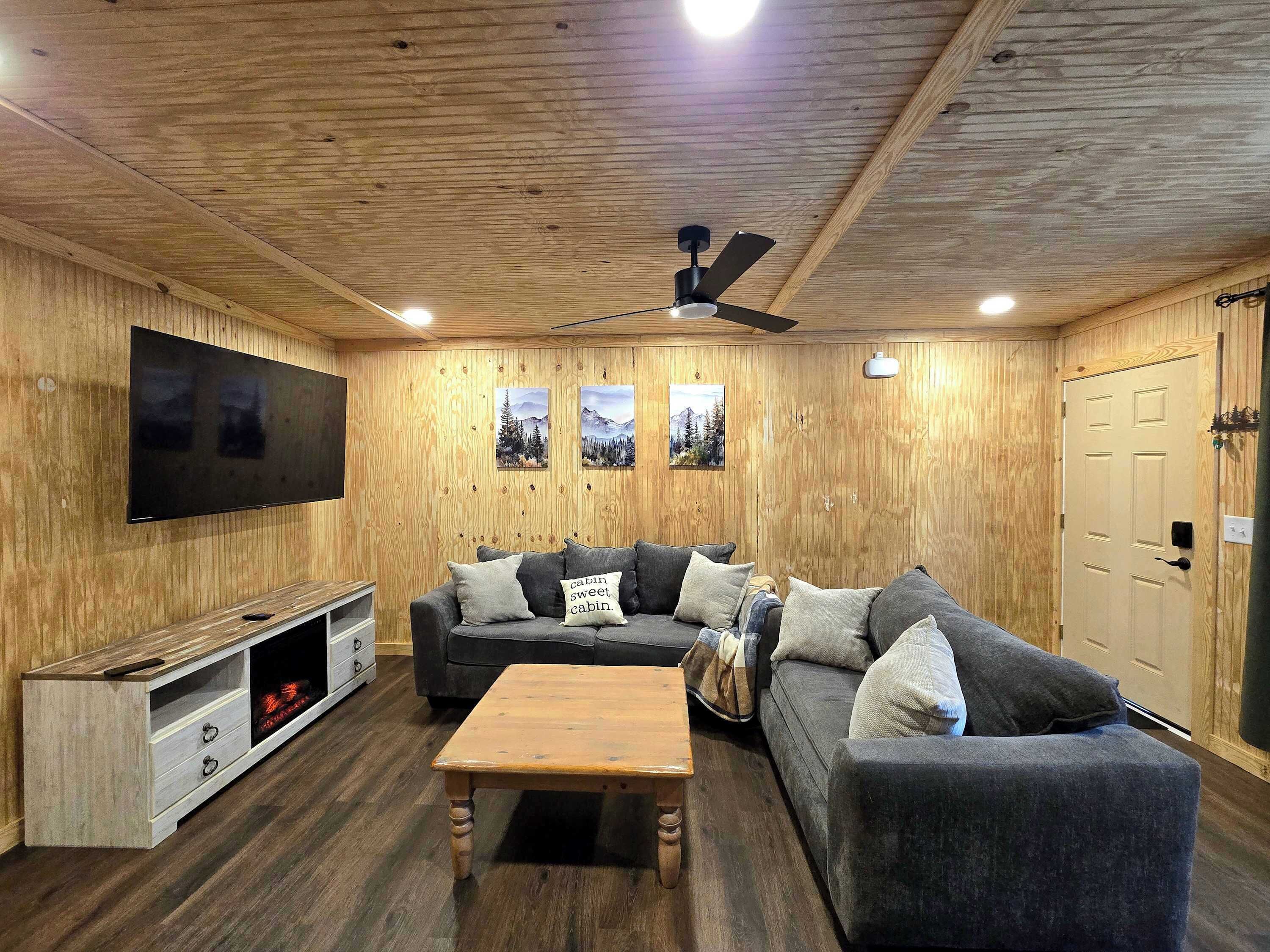 Quarto com painéis de madeira, televisão de tela plana, sofá, mesa de centro e ventilador de teto.