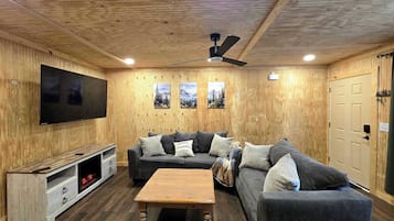 Quarto com painéis de madeira, televisão de tela plana, sofá, mesa de centro e ventilador de teto.
