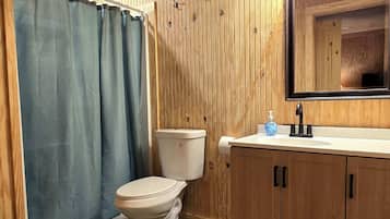 A wooden-paneled bathroom with a toilet, sink, and mirror.