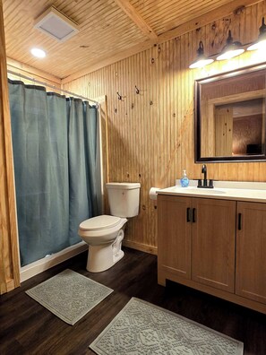 Une salle de bain aux murs lambrissés, équipée de toilettes, d’un lavabo et d’un miroir.