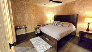 Un dormitorio con paneles de madera, una cama, dos lámparas de noche, un ventilador de techo y una alfombra estampada.