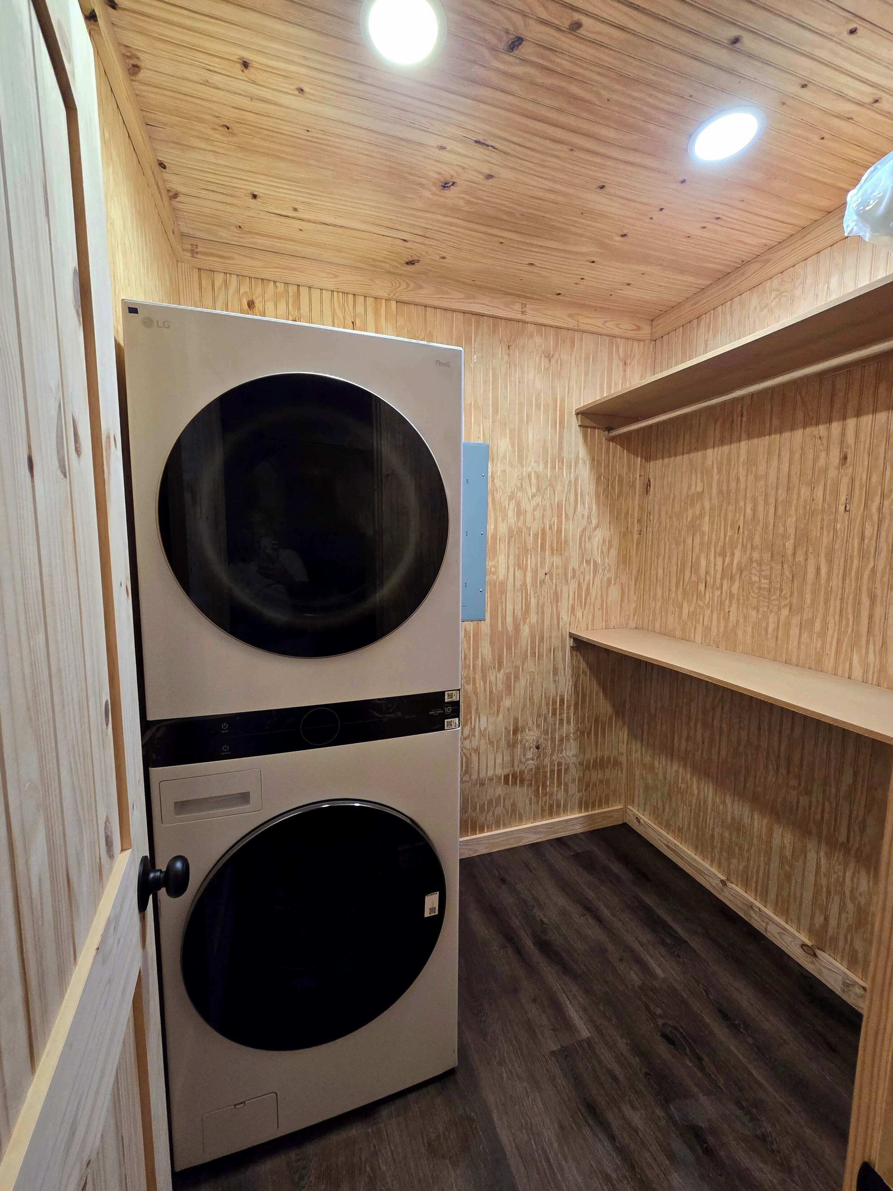 A laundry room with two stacked washing machines, wooden walls, and a ceiling with recessed lighting.