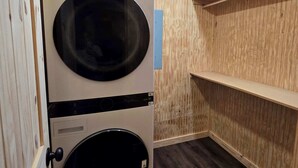 Un cuarto de lavandería con dos lavadoras apiladas, paredes de madera e iluminación empotrada en el techo.