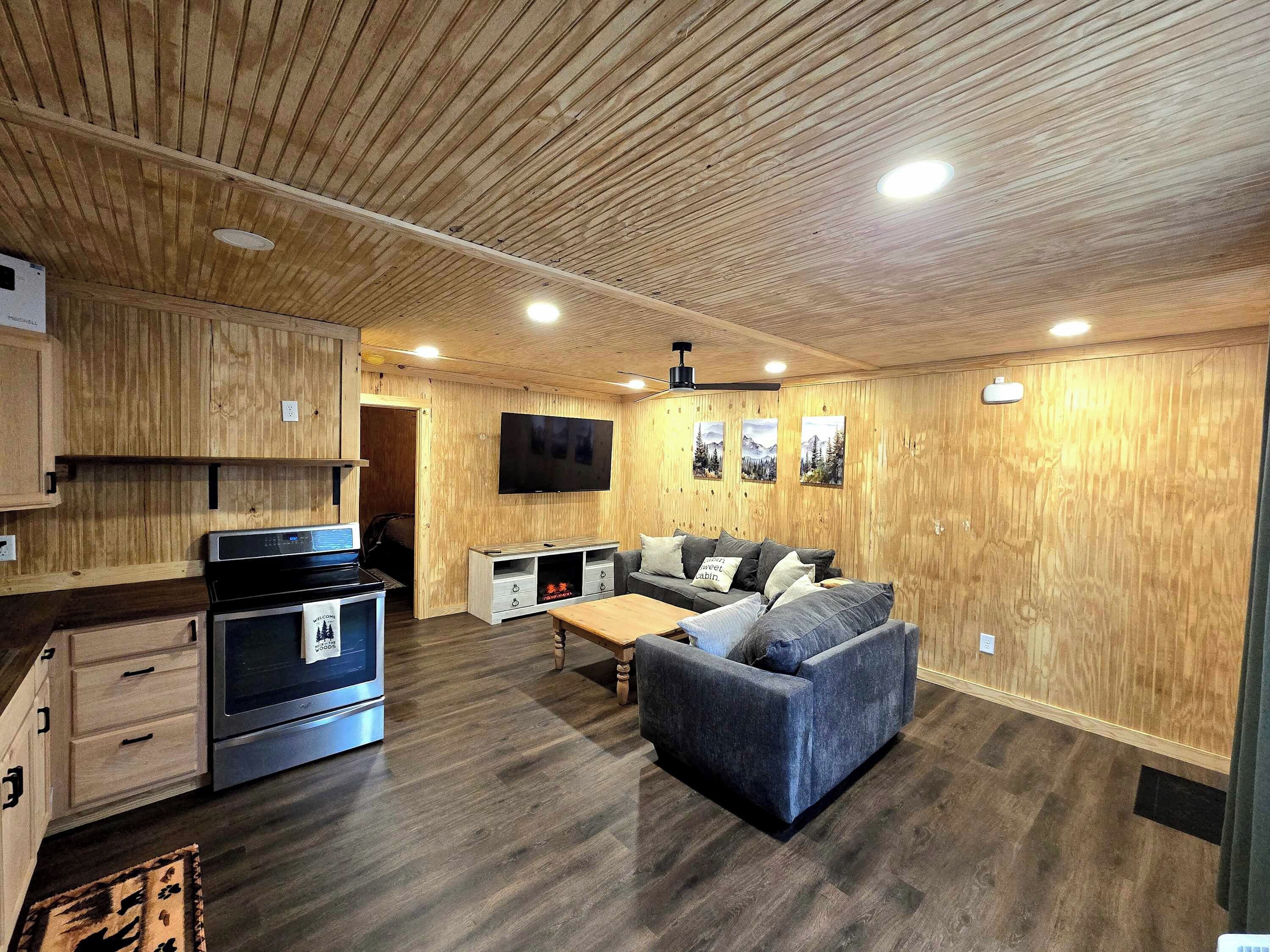 A modern kitchen with built-in appliances, a dining area with a sofa and table, and a flat-screen TV mounted on the wall.