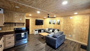 Una cocina moderna con electrodomésticos integrados, un comedor con sofá y mesa, y un televisor de pantalla plana montado en la pared.