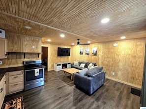 A modern kitchen with built-in appliances, a dining area with a sofa and table, and a flat-screen TV mounted on the wall. - The Lodge at Welch-The Cabin (Welch)