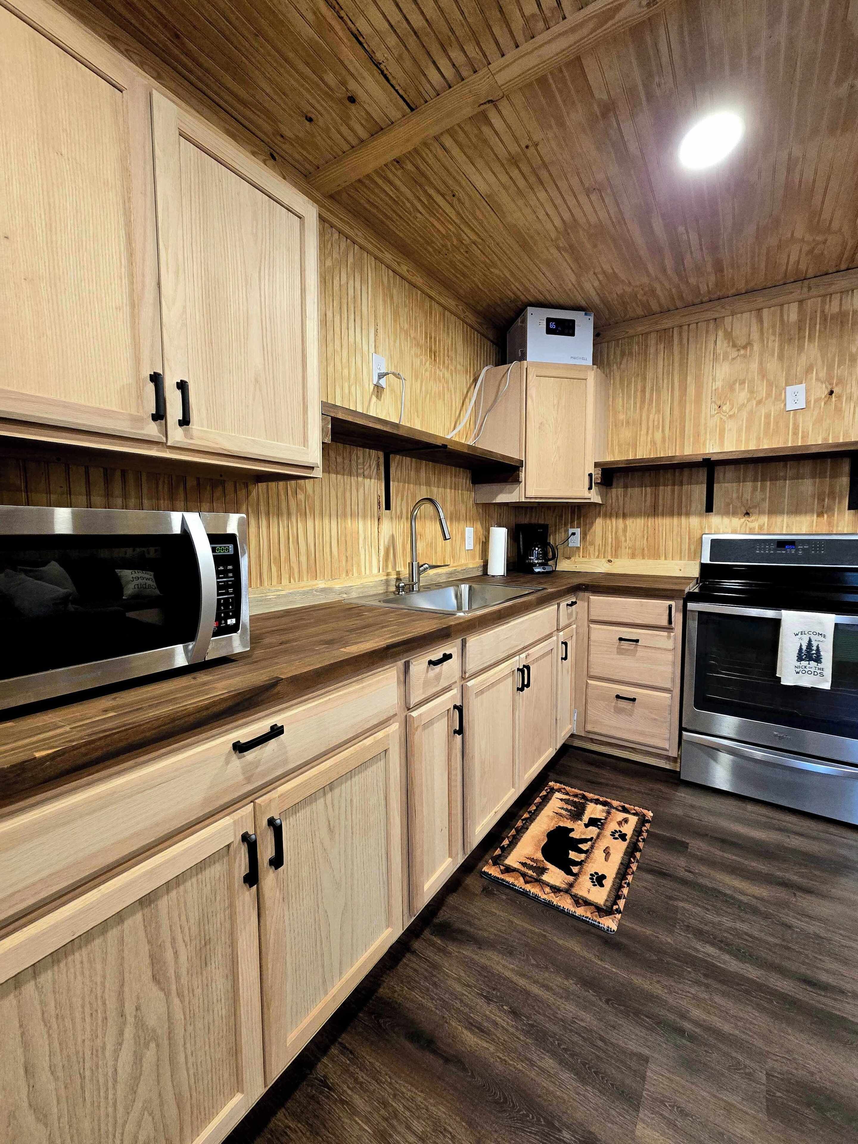 A modern kitchen with wooden cabinetry, stainless steel appliances, and a dark wooden floor.