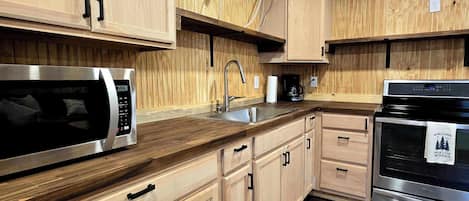 A modern kitchen with wooden cabinetry, stainless steel appliances, and a dark wooden floor.