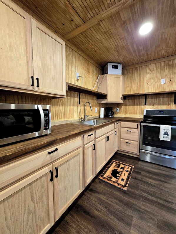 A modern kitchen with wooden cabinetry, stainless steel appliances, and a dark wooden floor.