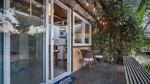 Uma área de estar coberta ao ar livre com cadeiras de vime e uma mesa, uma entrada com porta de vidro e um tapete de entrada com texto.