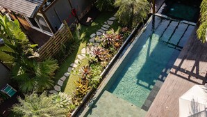 Piscina com deck de madeira, rodeada por vegetação exuberante e um caminho de pedra.