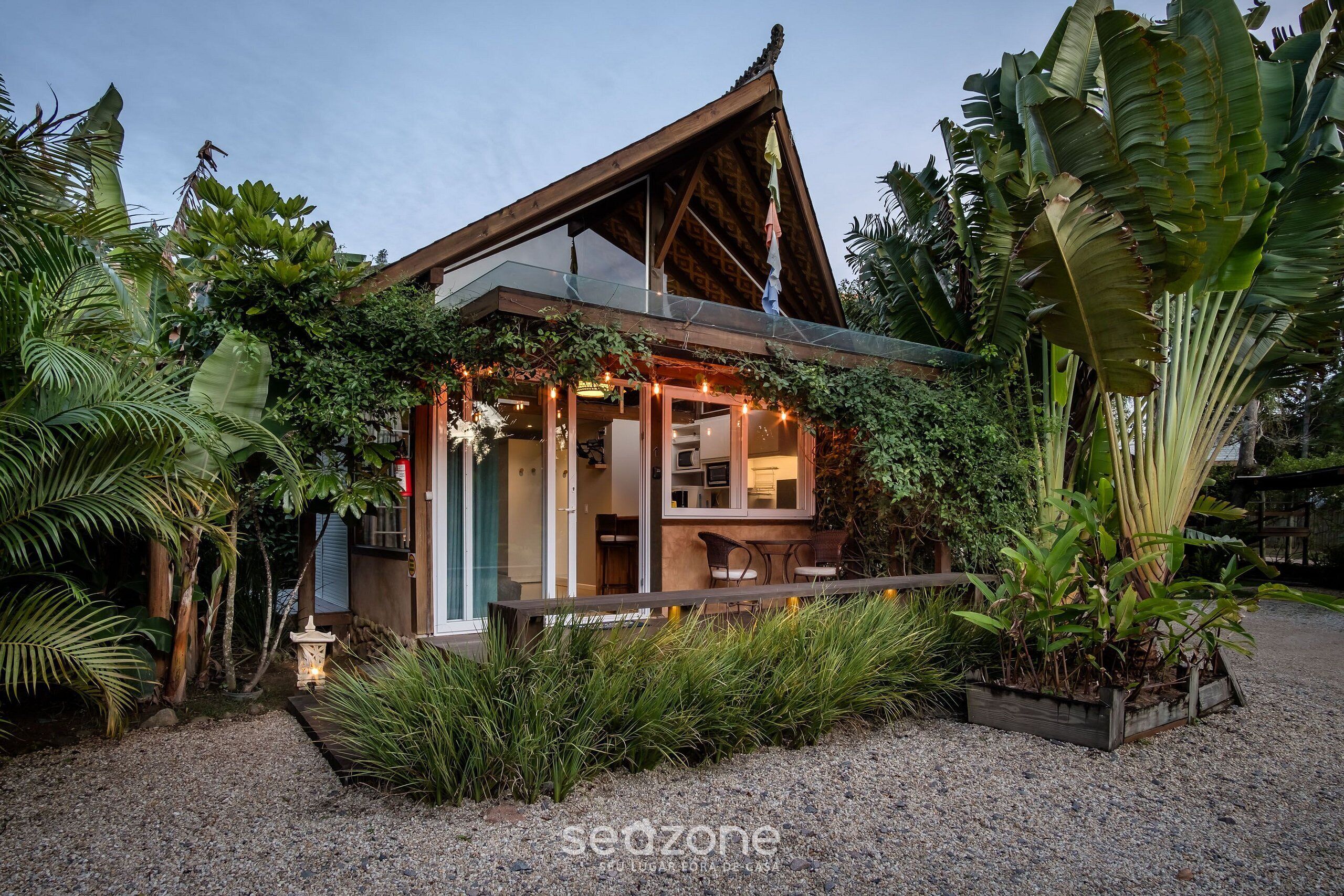 A house with a glass extension, surrounded by lush greenery and a gravel path.