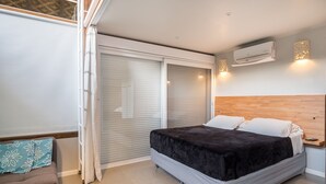 Quarto com cama, porta deslizante, ar condicionado e uma pequena mesa de cabeceira.