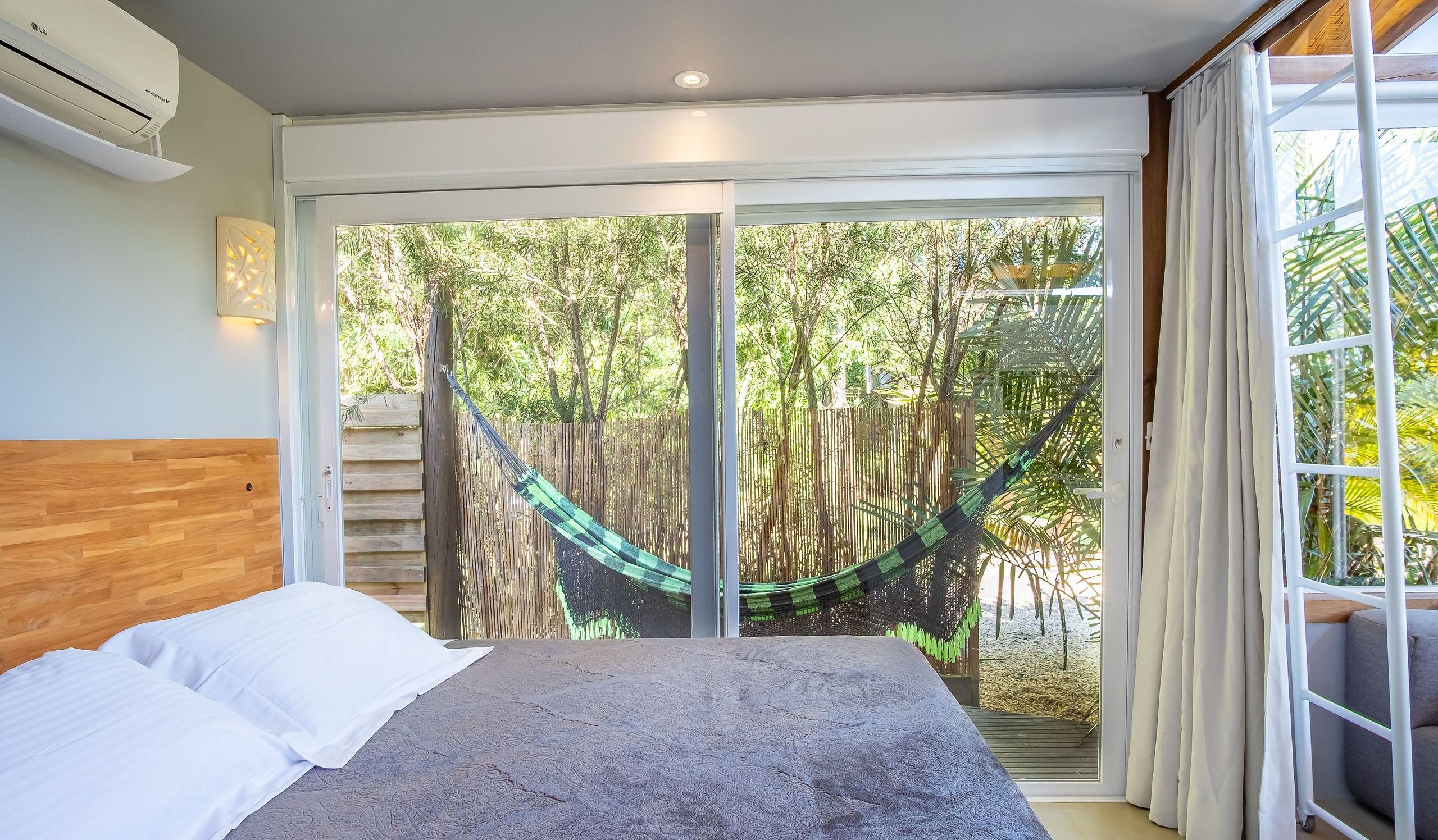 A bedroom with a bed, a hammock, and a view of a bamboo fence and trees.