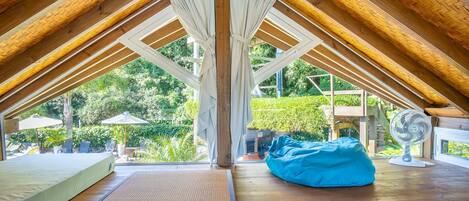 A room with a sloped ceiling, wooden beams, a bed, a blue bean bag, and a fan.