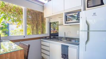 Cozinha compacta com micro-ondas, pia e pequena janela com vista para o verde.