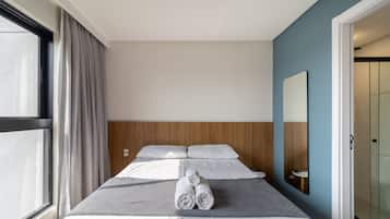 Una habitación de hotel con cama, espejo, ventana con cortinas y puerta.