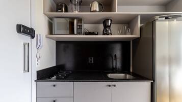 A compact kitchen with a black countertop, a stainless steel refrigerator, and a coffee maker on the shelf.
