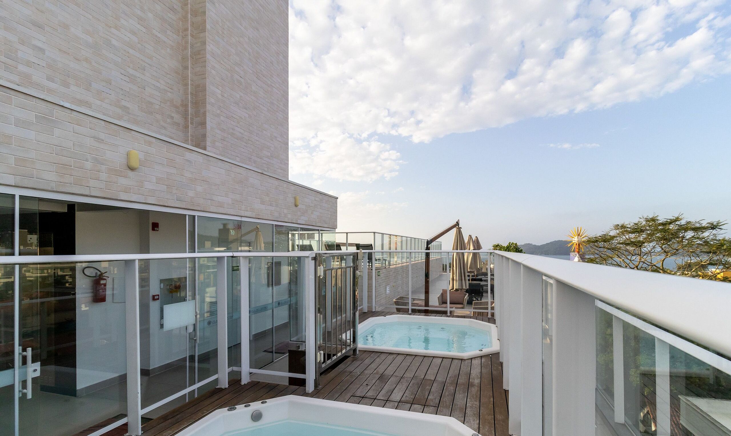 Eine Dachterrasse mit Whirlpool, Glasgeländern und Blick zum Himmel.