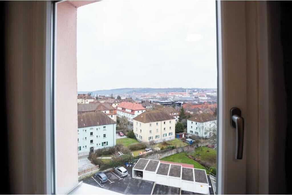 Une vue depuis une fenêtre, avec une poignée de porte, donnant sur un quartier résidentiel avec des immeubles et un parking.