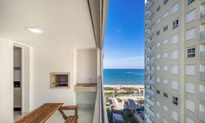A balcony with a wooden table and a small sink, overlooking a beach and a high-rise building. - 3BR Beachfront Condo w/ BBQ & Jacuzzi Shc0905 (Picarras)