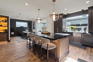 A modern kitchen with a central island, bar stools, pendant lighting, and dark cabinetry.