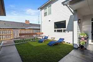A backyard with a lawn, a wooden deck, and a white house with a window.