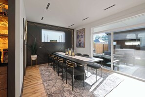 A modern dining area with a long table, chairs, and a view of the outdoors.