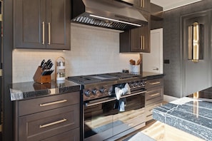 A modern kitchen with dark cabinetry, a stainless steel stove, and a built-in oven. - Luxury Designer Home -Private Oasis, Jacuzzi, Spa (Newberg)