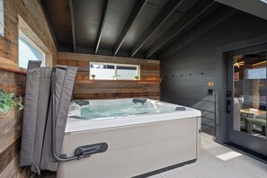 A hot tub in a modern outdoor setting with wooden walls and a glass door.