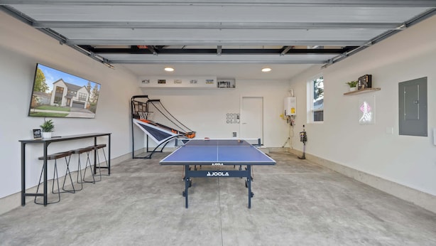 Ein Ping-Pong-Tisch in einer Garage mit einem Basketballkorb, einem Fernseher und einem Warmwasserbereiter.