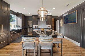 A modern kitchen with dark cabinetry, a central island, and bar stools. - Luxury Designer Home -Private Oasis, Jacuzzi, Spa (Newberg)
