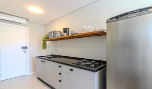 A modern kitchen with a stainless steel refrigerator, a built-in gas stove, and a microwave on a wooden shelf. - Complete Studio 650m From the Beach - BC - Dpr0003 (Balneário Camboriú)