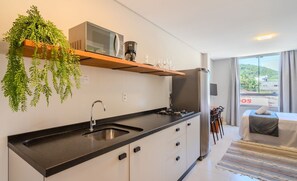 A modern kitchen with a black countertop, stainless steel sink, and a microwave. There is a hanging plant above the counter and a refrigerator to the right. - Complete Studio 650m From the Beach - BC - Dpr0003 (Balneário Camboriú)