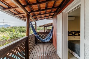 A wooden balcony with a hammock, a bed with a headboard, and a view of greenery.