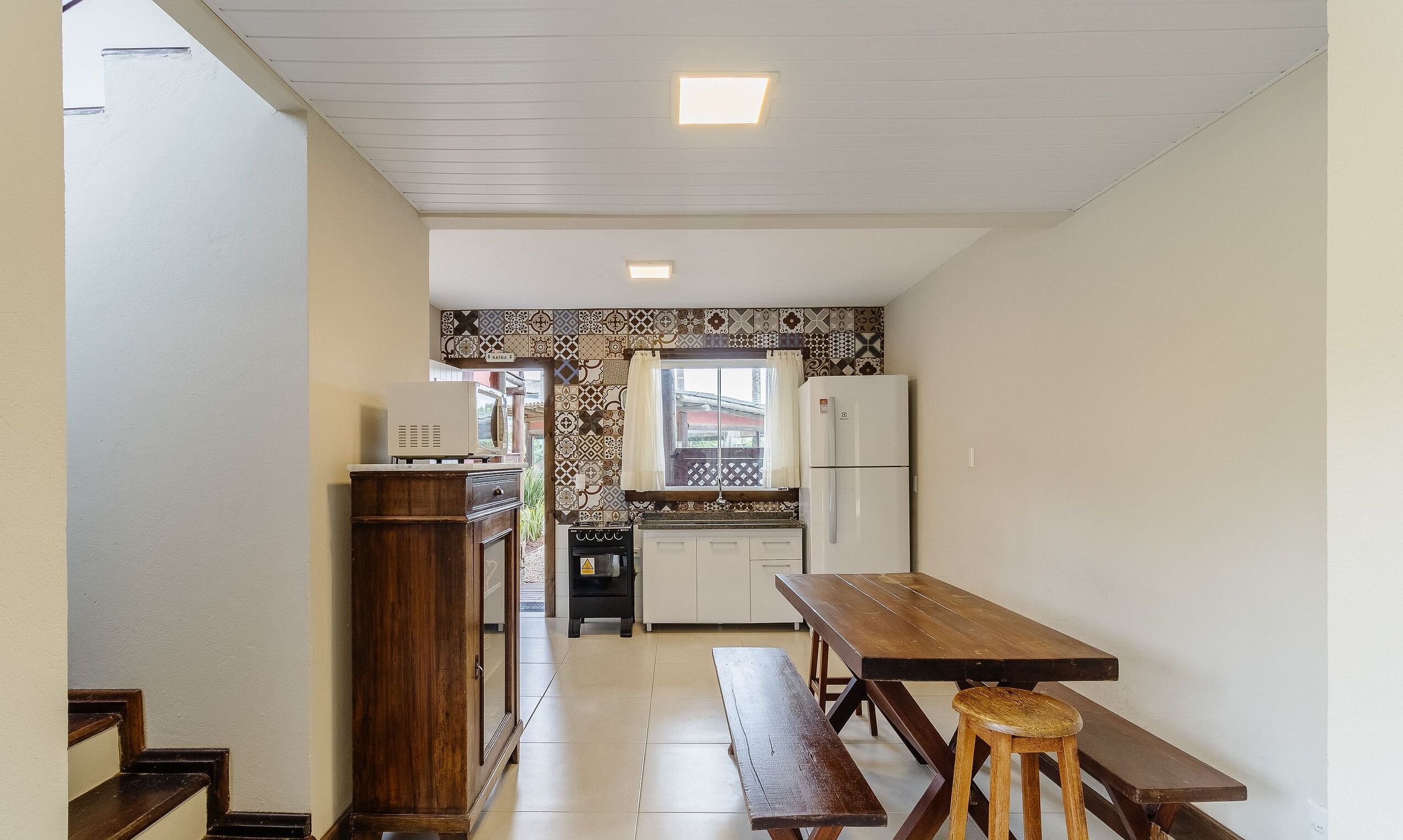 A compact kitchen with a wooden bench and table, a built-in oven, and a refrigerator.