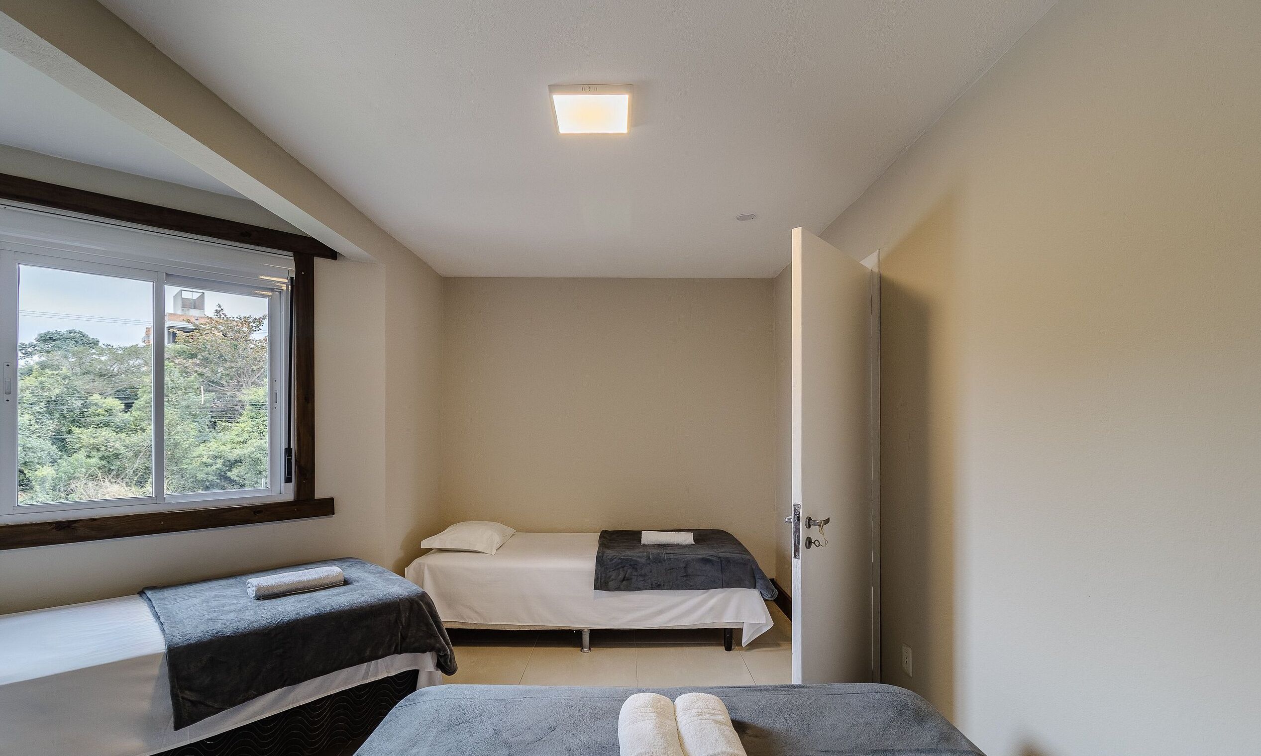 A small, single-room hotel room with a bed, a bench, and a window.
