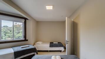 A small, single-room hotel room with a bed, a bench, and a window.