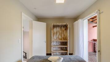 A narrow hallway leading to a room with a bed, a wooden wardrobe, and a door leading to an outdoor area.