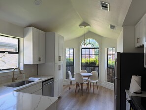 A kitchen with white cabinets, a marble countertop, a dining area with chairs, and a large window with a view of greenery. - Cozy Modern 3-bedroom house with AC in tranquil Fort Worth (Fort Worth)