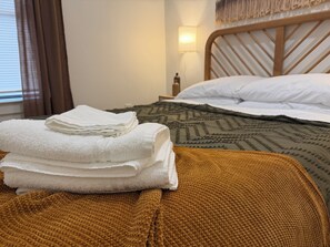 A neatly made bed with white linens and a brown knitted blanket, a bedside lamp, and a window with curtains. - Cozy Modern 3-bedroom house with AC in tranquil Fort Worth (Fort Worth)