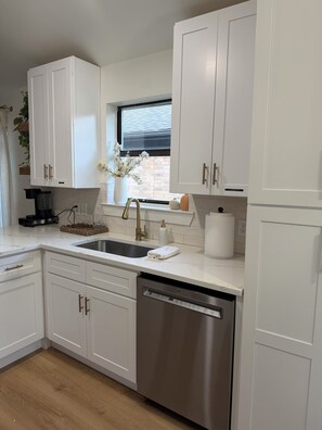 Una cocina moderna con armarios blancos, un lavavajillas de acero inoxidable y un ventanal con vistas al exterior.