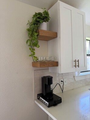 A kitchen with white cabinets, a coffee maker, and a potted plant on a wooden shelf. - Cozy Modern 3-bedroom house with AC in tranquil Fort Worth (Fort Worth)