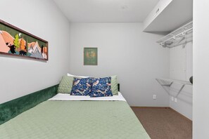 A bedroom with a bed, a green headboard, a wall-mounted shelf, and a painting.