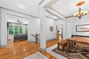 A spacious living area with a wooden floor, a dark-colored sofa, and a dining table with chairs. - Creekside Lodge 6bd 22 acres (Stilwell)