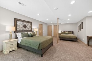 A bedroom with two beds, a nightstand, a lamp, and a decorative wall piece. - Creekside Lodge 6bd 22 acres (Stilwell)