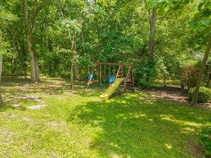 A playground with a swing set and a slide in a wooded area. - Creekside Lodge 6bd 22 acres (Stilwell)