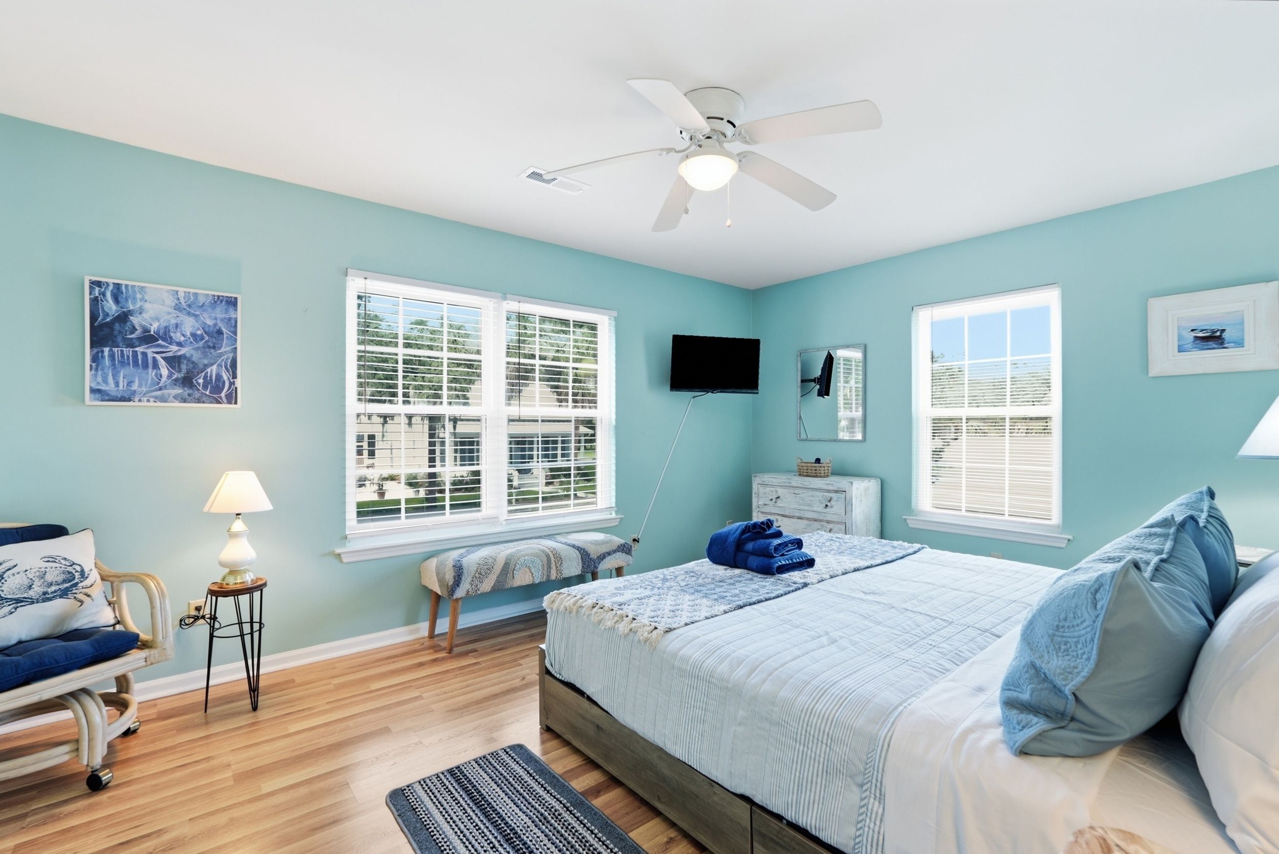 A bedroom with a bed, two windows, a ceiling fan, a TV, and a chair.