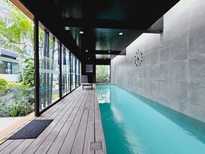 Een modern binnenzwembad met een houten terras, grote ramen en uitzicht op groen.